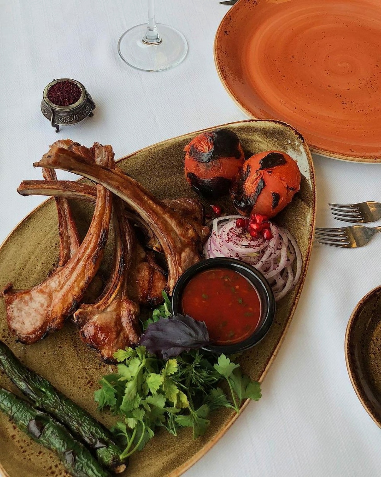 Grilled lamb chops with charred tomato, sumac onion and herbs on a stoneware plate at Sumakh in Baku
