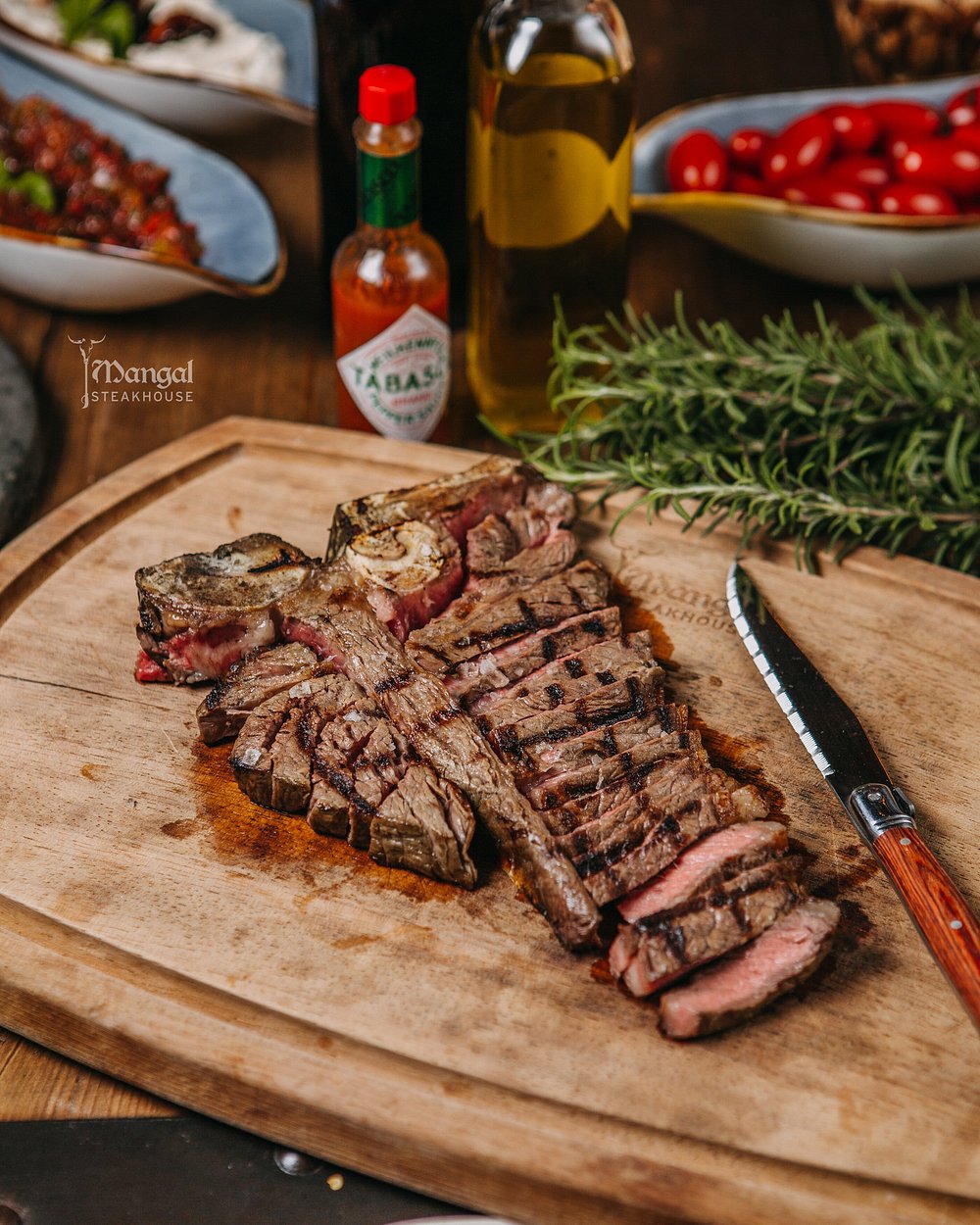 Sliced aged T-bone steak carved on a wooden board with rosemary and olive oil at Mangal in Baku
