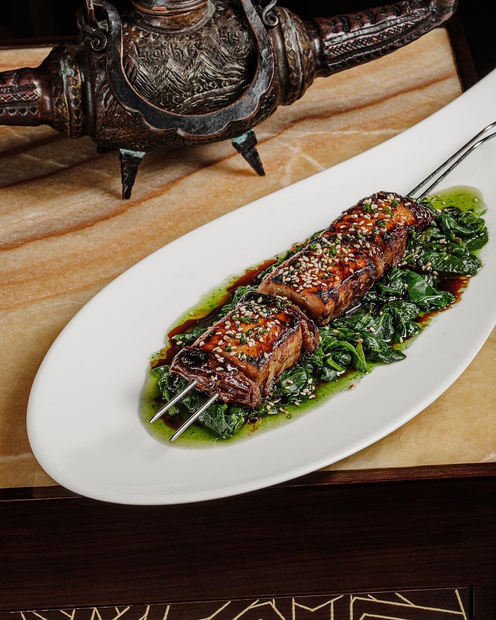 A glazed lamb skewer with sesame over wilted greens, plated at Shur in Baku