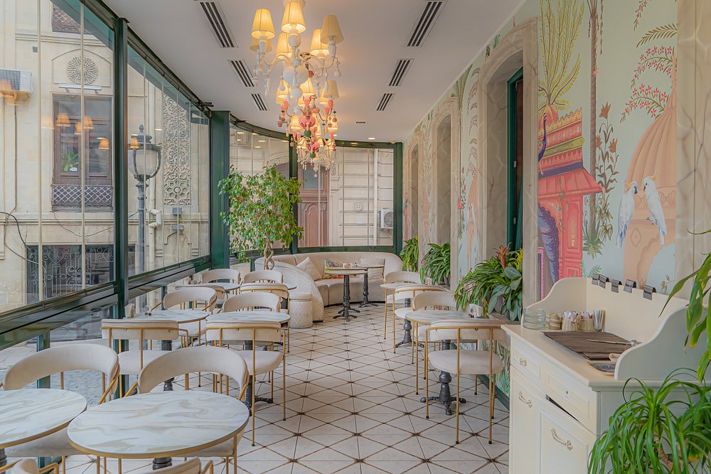 The glazed terrace at Merci Baku — chandelier, painted murals and marble café tables