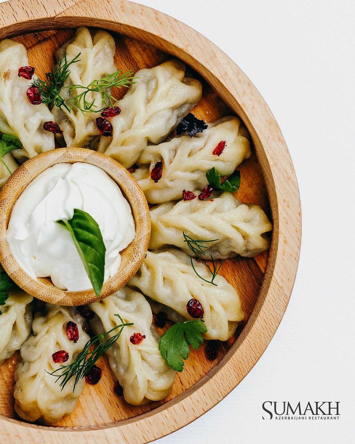 Azerbaijani dumplings arranged on a wooden board with sour cream, dill and barberry at Sumakh in Baku