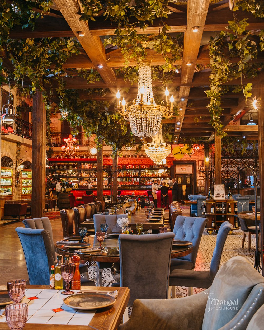 The dining room at Mangal in Baku, with crystal chandeliers, velvet seating, exposed wooden beams and trailing greenery above long set tables
