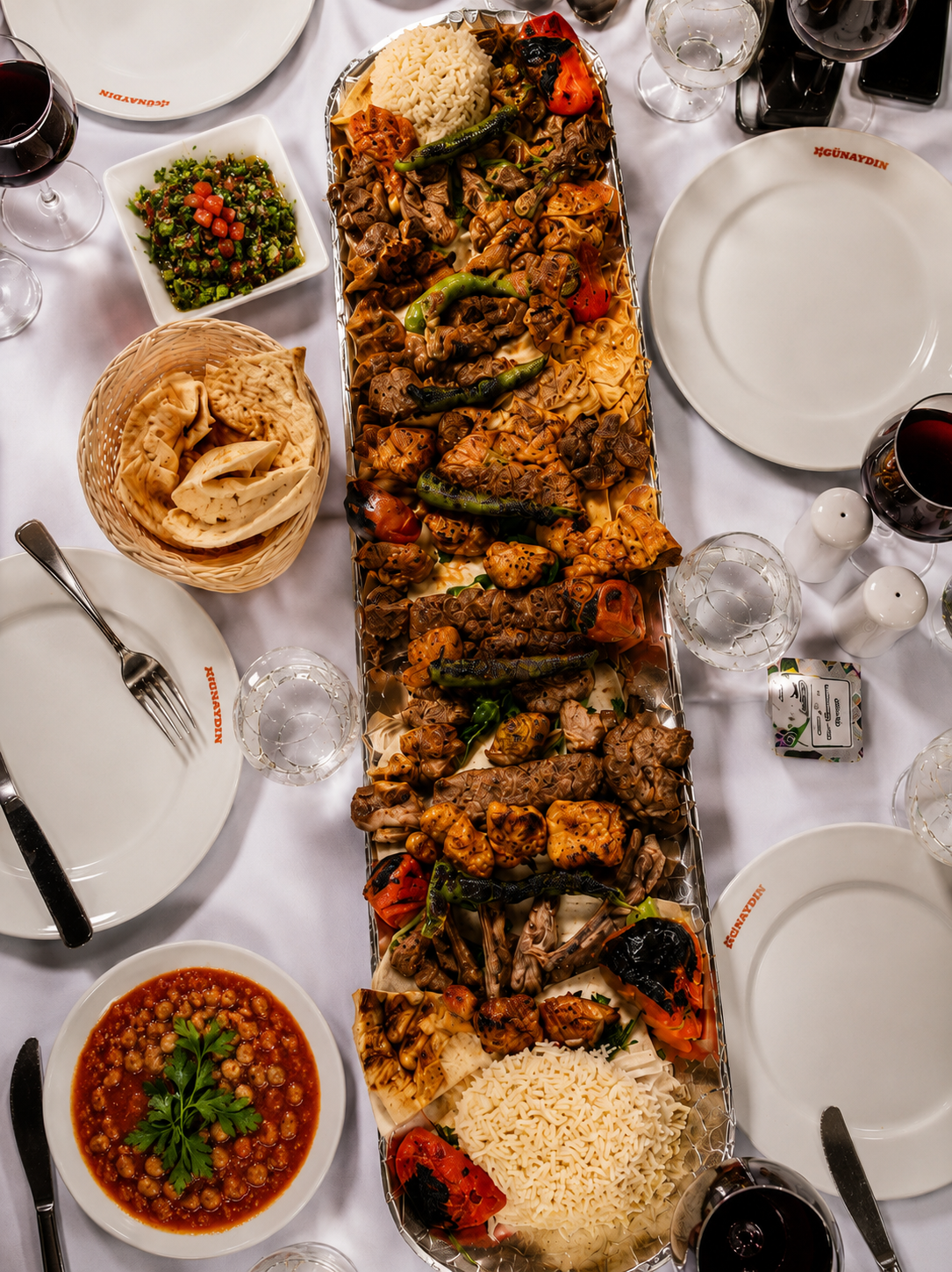 An overhead view of a long silver kebab platter for the table at Günaydın in Baku, with bread, salad and wine