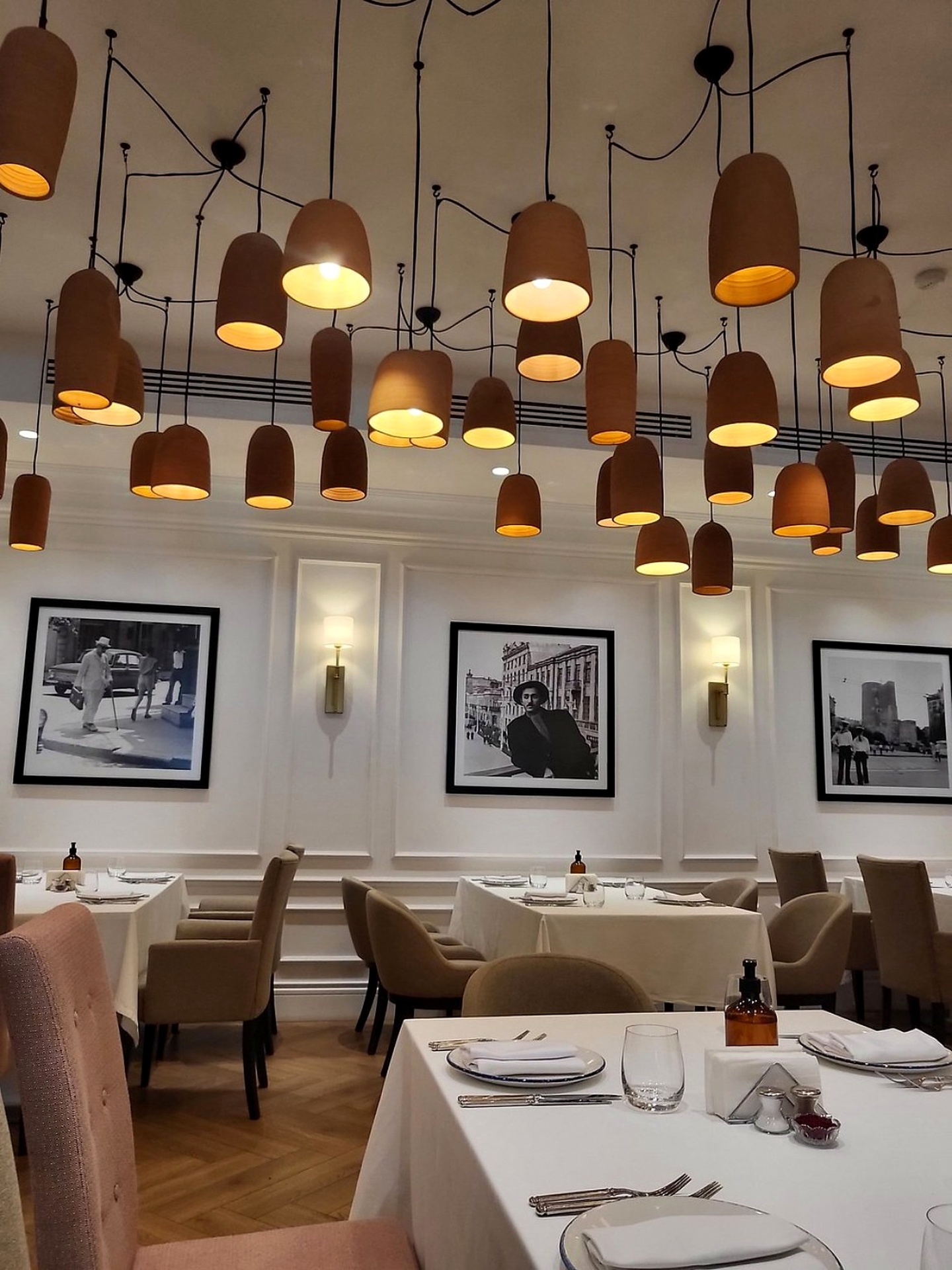 The dining room at Sumakh in Baku — terracotta pendant lights, white linen tables and framed black-and-white photographs of old Baku