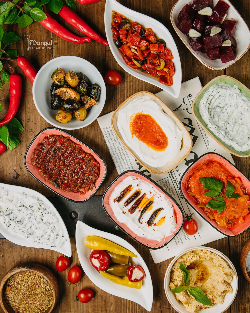 Cold starters of olives, roasted peppers, herbed yoghurt and hummus on a wooden table at Mangal in Baku